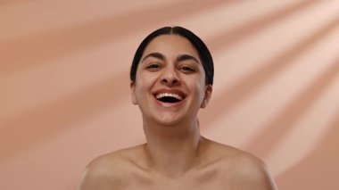 Neşeli bir kadın neşeli bir ifadeyle gülümserken yakalanır. Gülüşü, yumuşak bir arkaplan üzerine kurulmuş sıcaklığı ve pozitifliği yayıyor. Yavaş çekim