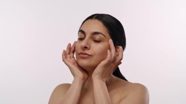 Kendine güvenen bir ifade ve doğal güzelliğe sahip bir kadın tarafsız bir arkaplanda rahat bir şekilde poz verir. Yavaş çekim