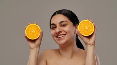 Gülümseyen bir kadın taze ve narenciye cazibesini vurgulayan iki canlı turuncu yarıya sahiptir. Yavaş çekim