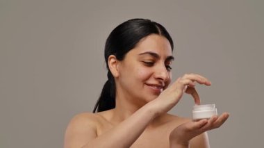 Bir kadın elinde bir krema kavanozu tutarken gülümsüyor. Işıl ışıl ifadesiyle güzelliği ve sağlığı teşvik ediyor. Yavaş çekim