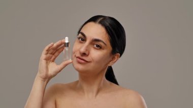 Bir kadın kendine güvenen bir serum şişesi tutuyor doğal güzelliği ve cilt bakımını gösteriyor. Yavaş çekim
