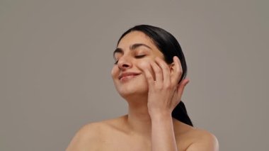 Temiz, sağlıklı tenine özenle dokunurken gülümseyen kendine güvenini ve doğal güzelliğini yansıtan kendine güvenen bir kadın. Yavaş çekim