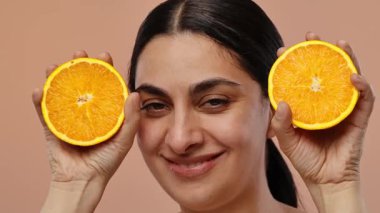 Gülümseyen bir kadın yüzüne iki taze portakal parçası dayamış, neşeli ve neşeli bir hava sergiliyor. Yavaş çekim