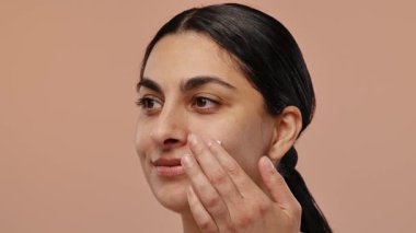 Bir kadın yüzüne nazikçe nemlendirici krem sürerek cilt sağlığını ve su kaybını rutin bir şekilde teşvik eder. Yavaş çekim