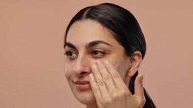 Bir kadın yüzüne nazikçe nemlendirici krem sürerek cilt sağlığını ve su kaybını rutin bir şekilde teşvik eder. Yavaş çekim