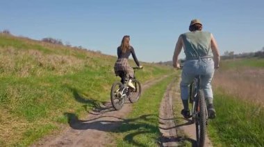 Bir çift doğa ile çevrili, doğa manzaralı bir patikada bisiklet sürüyor, kırsalda macera ve rahatlığın özünü yakalıyor. Arka plan, yavaş çekim