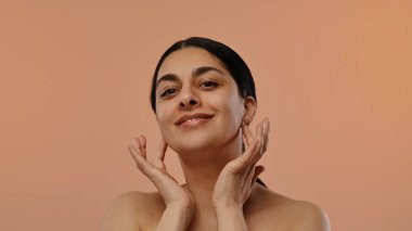 Yüzüne nazikçe dokunan bir kadın doğal güzelliğini ve özgüvenini ifade eder. Şeftali arkaplanının karşısında durur..