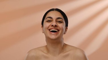 Neşeli bir kadın neşeli bir ifadeyle gülümserken yakalanır. Gülüşü, yumuşak bir arkaplan üzerine kurulmuş sıcaklığı ve pozitifliği yayıyor..