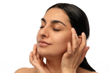 Huzurlu bir kadın yüzüne hafifçe dokunur, cilt rutininden zevk alır, gözleri kapalı, sakin bir şekilde..