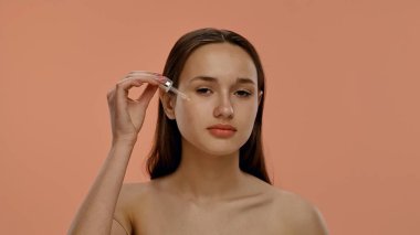 Bir kadın yüzüne serum uygulamak için bir damlatıcı kullanır. Cilt rutini, güzellik ve sağlığa önem verir, su kaybına odaklanır..