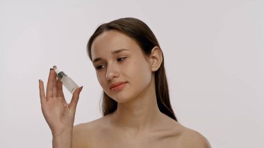 Bir kadın yüzüne serum uygulamak için bir damlatıcı kullanır. Cilt rutini, güzellik ve sağlığa önem verir, su kaybına odaklanır..