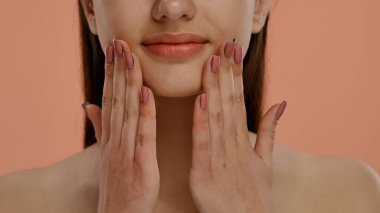 Resim, yüzüne nazikçe dokunan bir kadını tasvir ediyor. Tırnakları, cilt rengini tamamlayan Fransız manikür tasarımına sahip..