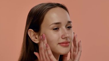 Doğal makyajlı genç bir kadın yüzüne nazikçe dokunarak sağlıklı cilt bakımını teşvik ediyor. Yavaş çekim
