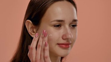 Doğal makyajlı genç bir kadın yüzüne nazikçe dokunarak sağlıklı cilt bakımını teşvik ediyor. Yavaş çekim