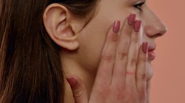 Doğal makyajlı genç bir kadın yüzüne nazikçe dokunarak sağlıklı cilt bakımını teşvik ediyor. Yan görünüm, yakın çekim, yavaş çekim