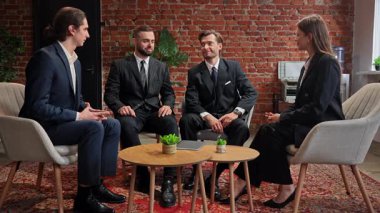 İş kıyafeti giymiş dört kişi, tuğla duvarlı ve modern dekorlu şık bir ofiste buluşuyor. Yavaş çekim.