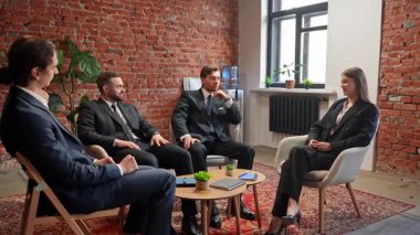 Dört iş adamı, duvarları tuğlalı ve bitkileri olan şık bir ofiste strateji tartışan bir toplantıya giriyorlar. Yavaş çekim.