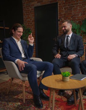 İki işadamı bir ofiste oturmuş arkadaşça sohbet ediyorlar, bu da olumlu bir etkileşim olduğunu gösteriyor..