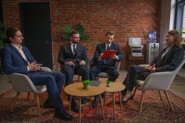 Bir grup profesyonel, modern bir ofiste duvarları tuğladan yapılmış belgeleri tartışıyorlar..