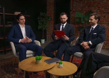 Bir grup profesyonel, modern bir ofiste duvarları tuğladan yapılmış belgeleri tartışıyorlar..