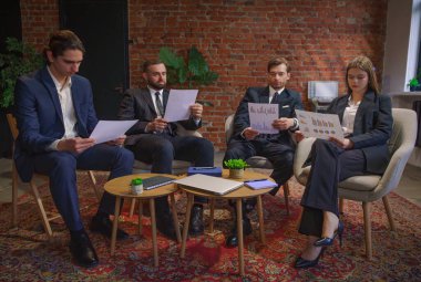 Bir grup iş adamı, tuğla duvarlı çağdaş bir ofiste mali belgeleri inceliyor..