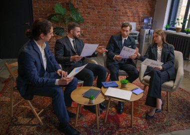 Bir grup iş adamı, tuğla duvarlı çağdaş bir ofiste mali belgeleri inceliyor..