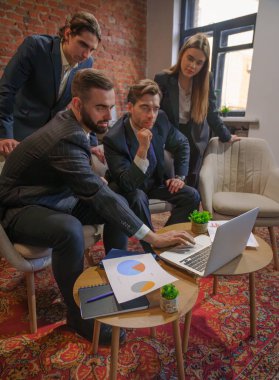 Çağdaş bir ofiste dizüstü bilgisayardaki verileri analiz eden bir grup profesyonel iş toplantısına katıldı..