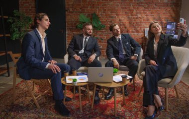 Bir iş ekibi modern ofis ortamında toplantı yapıyor. Bir kadın iş arkadaşlarıyla selfie çekiyor..