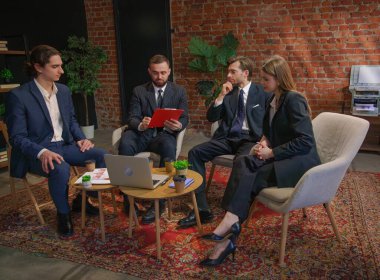 Bir grup profesyonel, modern bir ofiste duvarları tuğladan yapılmış belgeleri tartışıyorlar..