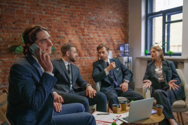 Bir grup profesyonel iş adamı bir toplantıya katılıyor. Diğerleri tartışırken, biri telefonda konuşuyor..