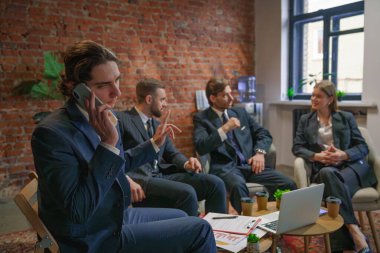 Bir grup profesyonel iş adamı bir toplantıya katılıyor. Diğerleri tartışırken, biri telefonda konuşuyor..