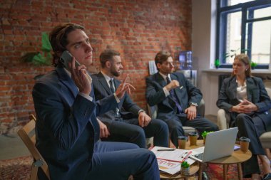 Bir grup profesyonel iş adamı bir toplantıya katılıyor. Diğerleri tartışırken, biri telefonda konuşuyor..