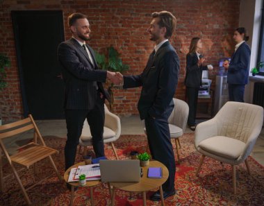 Modern bir ofiste iş arkadaşları el sıkışıyor, profesyonel bir çevre ve takım çalışması geliştiriyor..