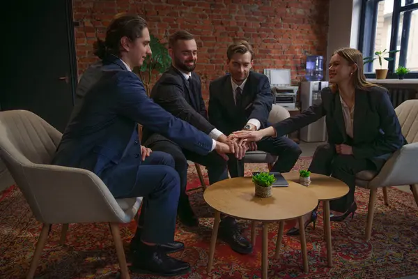 Resmi giyinmiş dört iş adamından oluşan bir grup, birliği simgeleyen bir masanın üzerinde el ele tutuşuyor..