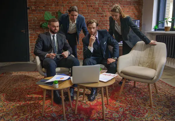 Çağdaş bir ofiste dizüstü bilgisayardaki verileri analiz eden bir grup profesyonel iş toplantısına katıldı..