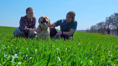 Doğa ve manzaralı bir köy manzarası ile çevrili çimenli bir tarlada köpeğiyle güneşli bir günün tadını çıkaran iki insan..