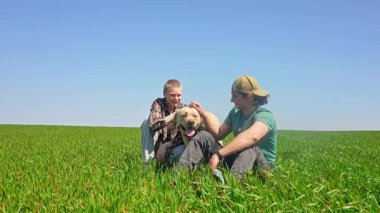 Doğa ve manzaralı bir köy manzarası ile çevrili çimenli bir arazide köpeğiyle güneşli bir günün tadını çıkaran iki insan. Yavaş çekim