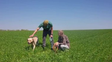 Doğa ve manzaralı bir köy manzarası ile çevrili çimenli bir tarlada köpeğiyle güneşli bir günün tadını çıkaran iki insan..