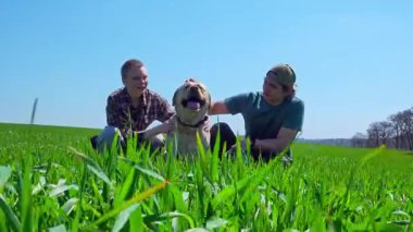 Doğa ve manzaralı bir köy manzarası ile çevrili çimenli bir tarlada köpeğiyle güneşli bir günün tadını çıkaran iki insan..