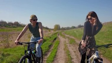 Bir çift, doğa tarafından çevrelenmiş, doğa manzaralı bir patikada bisiklet sürüyor, kırsal kesimde macera ve rahatlığın özünü yakalıyor..