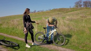 Bir çift bisiklet tamir ederken görüldü. Manzaralı bir ortamda, takım çalışmasını ve doğayı ön plana çıkarıyor..