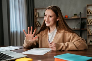Çevrimiçi bir toplantıya katılan gülümseyen genç bir kadın eğitim materyalleriyle eğitici bir ortam sunuyor..