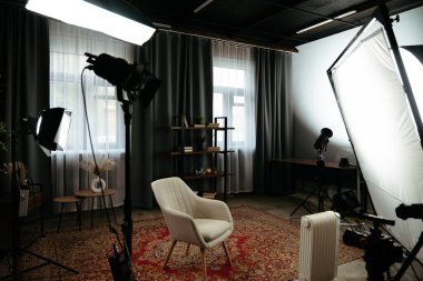 Sahne arkasında. Profesyonel ışıklandırma, modern bir sandalye ve şık bir dekorun yer aldığı iyi organize edilmiş bir fotoğraf stüdyosu. Portre oturumları için ideal.