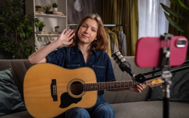 Evde gitar dersi veren bir kadın, kamera ve mikrofon kullanarak eğitim içeriği yaratıyor..