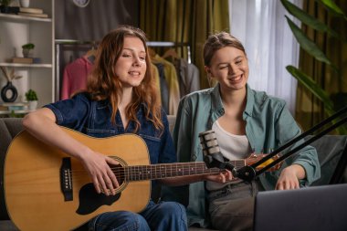 İki kadın kanepede rahat bir şekilde otururken mikrofona oturup gitar çalmayı ve şarkı söylemeyi seviyor..