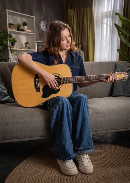 Genç bir kadın kanepede rahatça oturur, ustaca akustik gitar çalar, rahatlatıcı bir atmosfer yaratır..