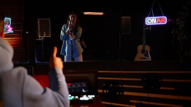 Bir kadın canlı neon ışıklarıyla çevrili bir stüdyoda mikrofona tutkuyla şarkı söylüyor..