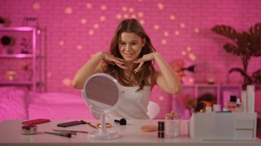 Neşeli bir birey makyaj masasında oturuyor. Güzellik ürünleriyle çevrili. Büyüleyici bir video seansına hazır..