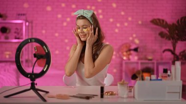 Bir güzellik blogcusu cilt bakımını gösterirken göz bandı altında altın yapıştırıyor. Mekan canlı ve neşeli..