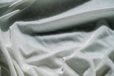 Beyaz kumaşın detaylı bir görüntüsü, dokulu bir yüzeyi ve ışıltılı detayları var. Karmaşık tasarımını sergiliyor..